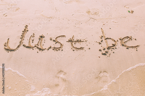 Close up of a phrase Just Be written in the sand