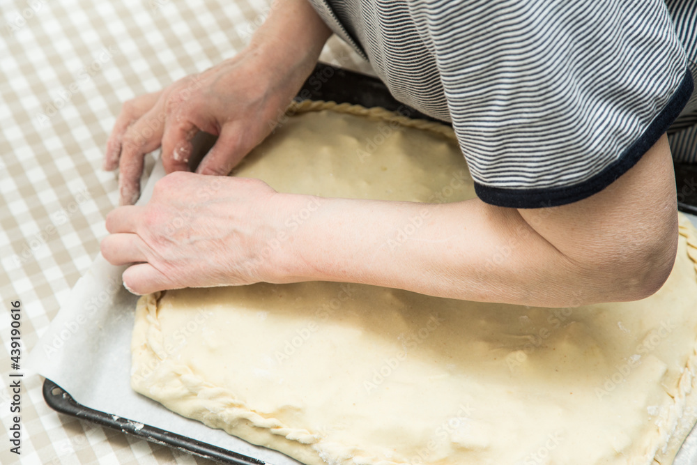 The hands of an adult elderly woman are preparing a dough pie. The fingers of the hands fasten the edges of the dough to each other. The hands of an adult elderly woman are preparing a dough pie. The fingers of the hands fasten the edges of the dough to each other.