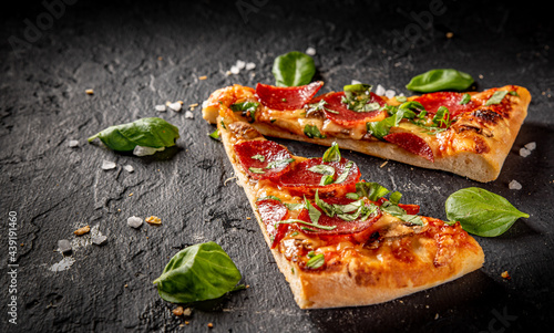 two slice of flatbread Pepperoni Pizza with Mozzarella cheese, salami, Tomato sauce, pepper, Spices. Italian pizza on Dark grey black slate background