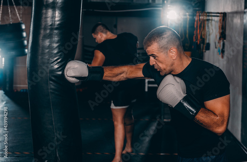 Concentrated young sportsman training thai boxing with punching bag