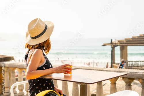 Summer vacation lifestyle. Young caucasian girl in a hat having a soda next to the beach