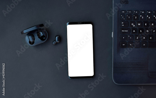 Black smartphone, laptop and headset on black background. Top view with copy space. .