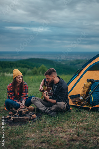 Young couple of campers sitting next to the tent while playing guitar