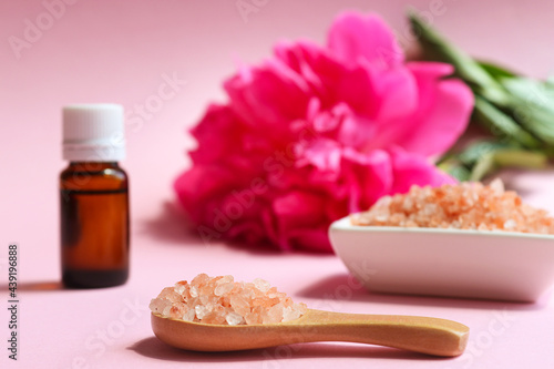 Beauty and spa concept. Pink himalayan salt close-up on a wooden spoon, essential oil and peony flower in the background. Selective focus