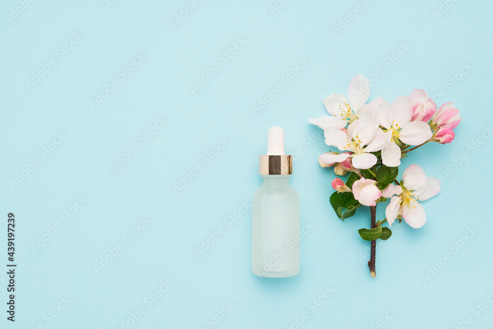 Glass dropper bottle and apple tree blossom on a blue background Glass dropper bottle and apple tree blossom on a blue background