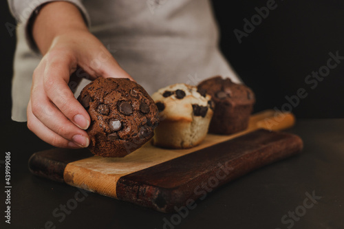 pastry chef presenting homemade vanilla and chocolate chips muffins  on a black background with sugar