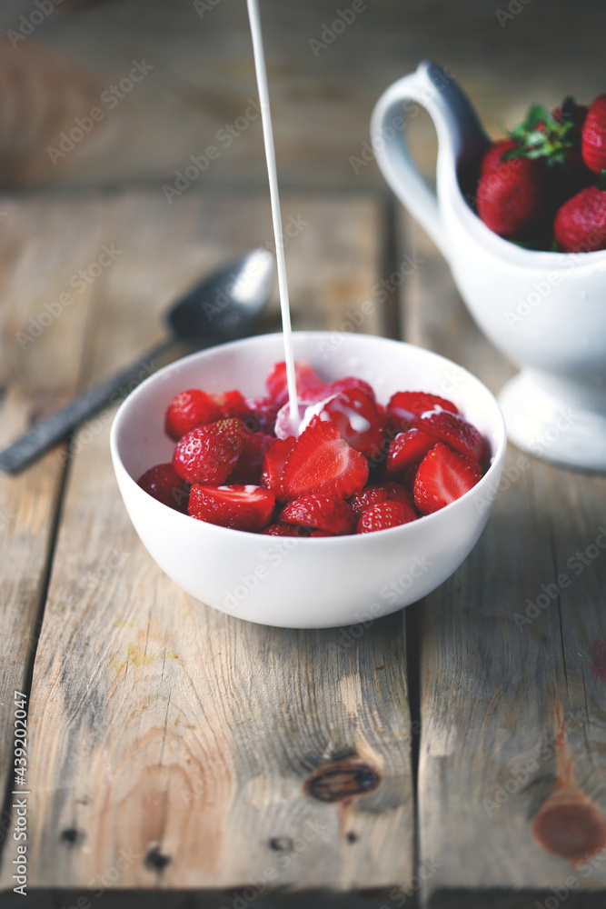 A stream of milk is poured into a bowl of strawberries. Cooking strawberry dessert with milk. A stream of milk is poured into a bowl of strawberries. Cooking strawberry dessert with milk.