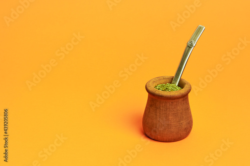 argentine wooden mate cup on orange background with yerba mate inside and straw photo