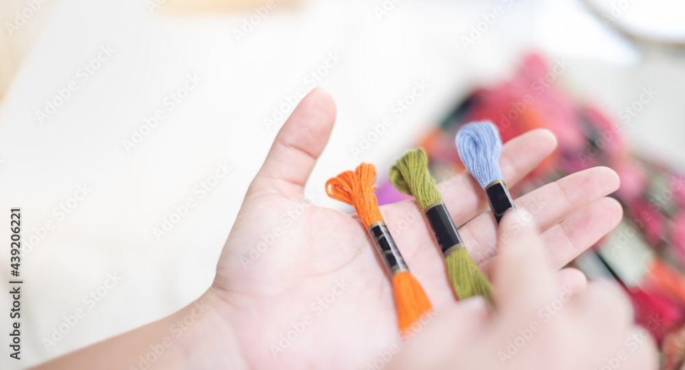 Close up hands of tailor woman holding many threads of different colors on table and prepare to use with white cotton and frame wood. Close up hands of tailor woman holding many threads of different colors on table and prepare to use with white cotton and frame wood.