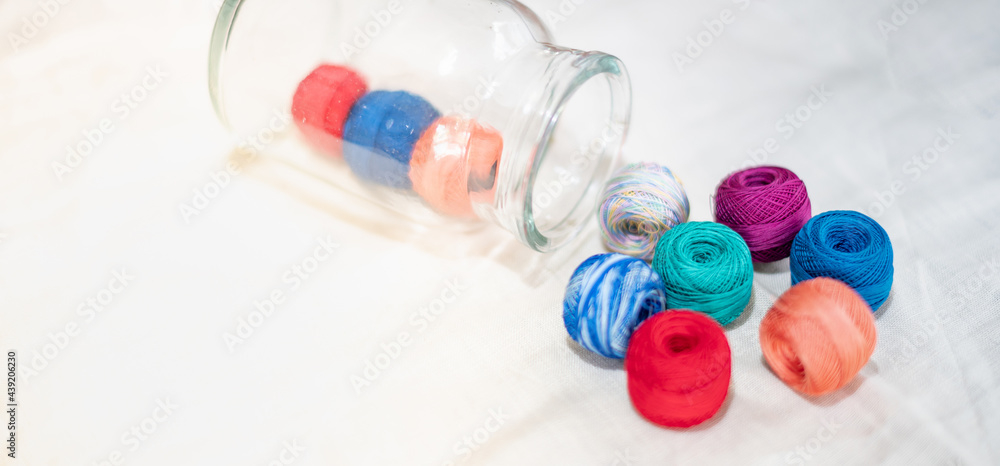 Colored balls of yarn in the glass bottle and put on the white cotton background Colored balls of yarn in the glass bottle and put on the white cotton background