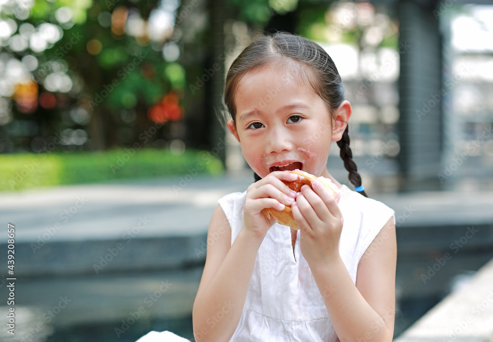 Happy Asian little girl eating bread with Stuffed Strawberry-filled dessert and Stained around her mouth in garden outdoor. Happy Asian little girl eating bread with Stuffed Strawberry-filled dessert and Stained around her mouth in garden outdoor.