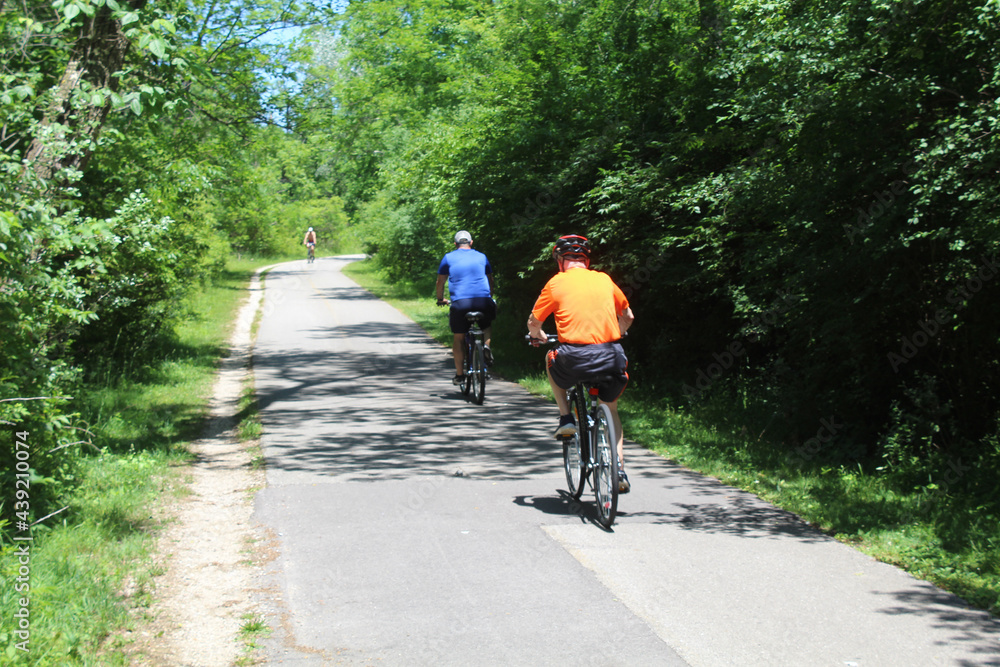 Three men riding bicycles on the North Branch Trail in summer on a sunny day in Niles, Illinois Three men riding bicycles on the North Branch Trail in summer on a sunny day in Niles, Illinois