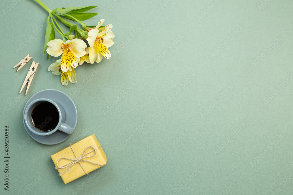 Yellow gift box, flower bouquet, cup of coffee on green background. flat lay, top view, copy space
