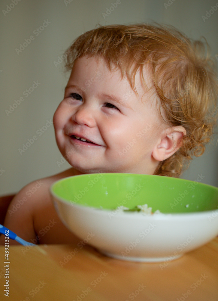 Portrait of cute Caucasian child kid with spoon. Hungry messy baby with plate after eating puree. Portrait of cute Caucasian child kid with spoon. Hungry messy baby with plate after eating puree.