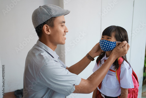 father helping her daughter to wear a mask before going to school in the morning to prevent from a covid 19 virus