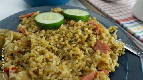 Fried rice served with fresh tomatoes and meatballs in a green tosca ceramic plate and pickles on a white bowl on a white background