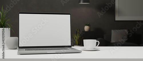 Laptop with mock-up screen on white table with a cup and decorations, 3D rendering