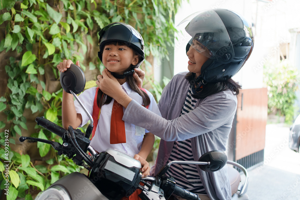mother taking her daughter to school by motorcycle in the morning. asian primary student wearing uniform going back to school mother taking her daughter to school by motorcycle in the morning. asian primary student wearing uniform going back to school