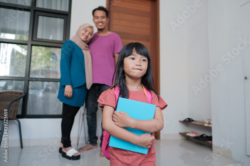happy portrait of beautiful asian primary student going to school in the morning while parent in the background