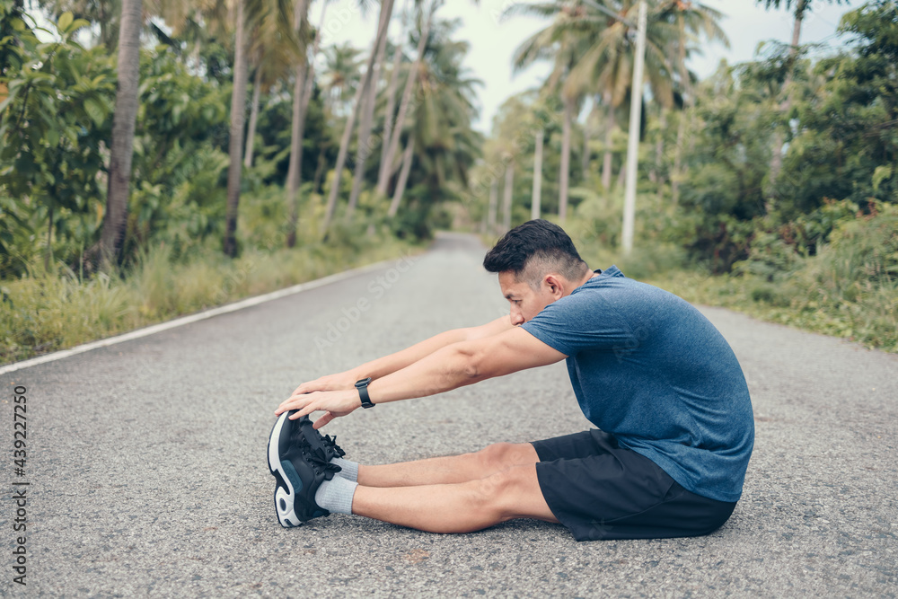 young man stretching in the park before running. Young man workout before fitness training at the park. Healthy and exercise young man warming up on the road in the forest. young man stretching in the park before running. Young man workout before fitness training at the park. Healthy and exercise young man warming up on the road in the forest.