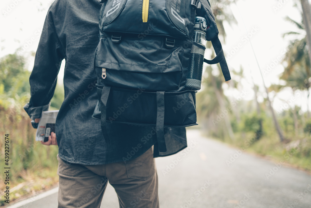 rear view of man with backpack hold passport and map hiking and walking on the road in forest. Backpack travel concept. rear view of man with backpack hold passport and map hiking and walking on the road in forest. Backpack travel concept.