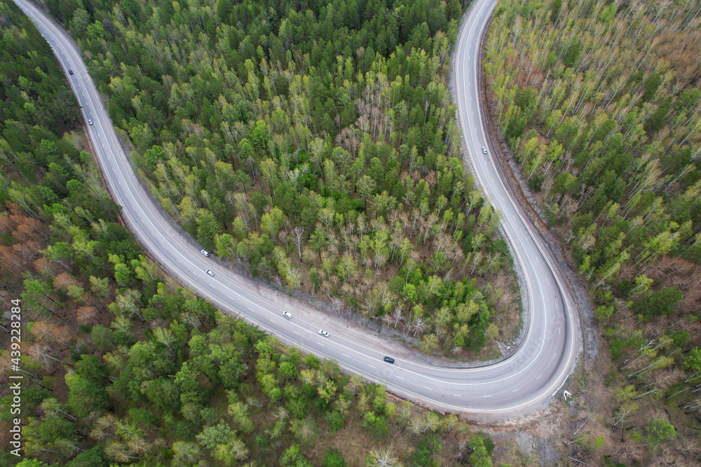 Cars drive on an asphalt road through the forest. Aerial view of the serpentine highway.