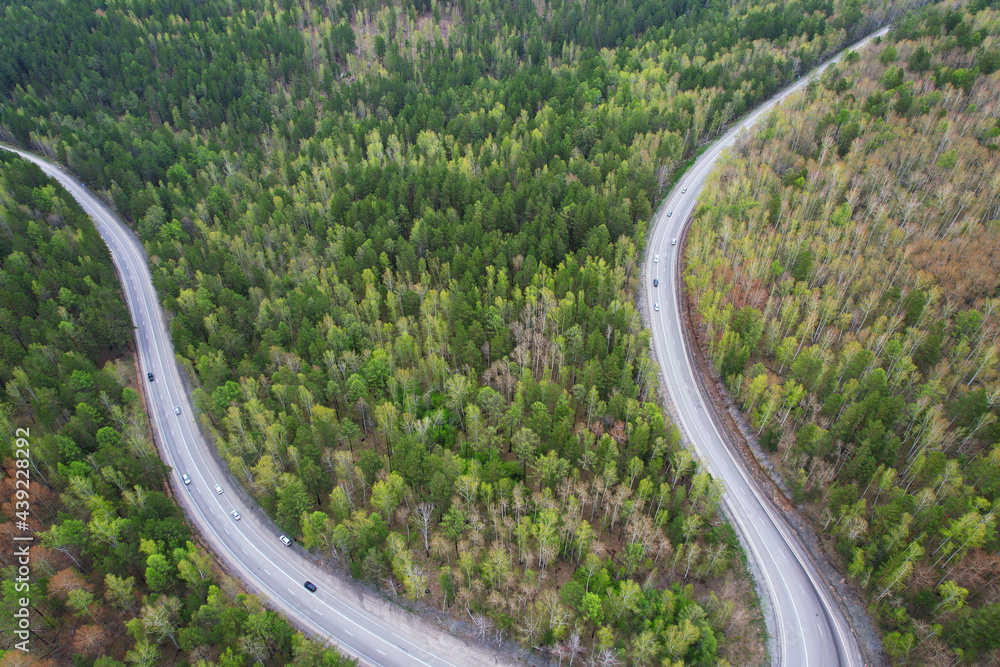 Aerial view of the serpentine highway. Cars drive on a road through the spring forest. Aerial view of the serpentine highway. Cars drive on a road through the spring forest.