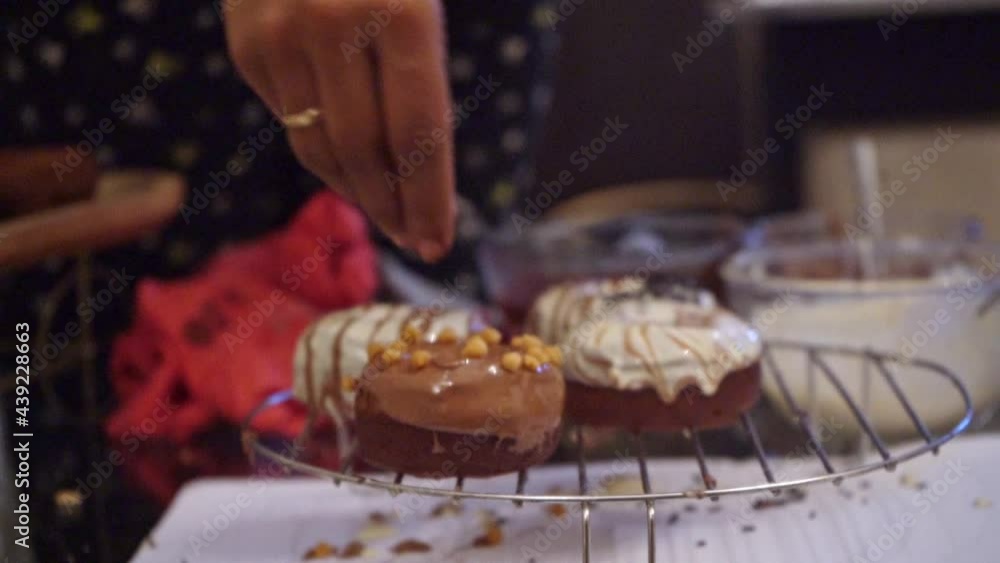 Baker Sprinkles The Glazed Donut With Nuts On The Cooling Rack. medium shot Baker Sprinkles The Glazed Donut With Nuts On The Cooling Rack. medium shot