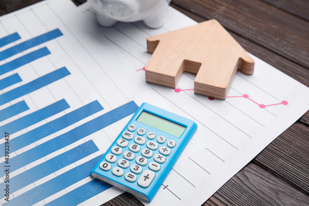 Calculator with house figure and charts on wooden background, closeup Calculator with house figure and charts on wooden background, closeup