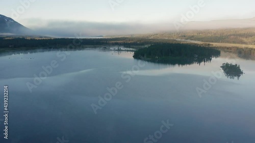 Early morning flight above a Nedre Fiplingvatnet lake. Through misty air a spectator sees the blackness of a still lake, pines not yet touched with sun rays, a dense forest hidden in the background. photo