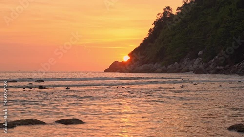 A dramatic orange sun dips behind a mountain along the coastline. photo