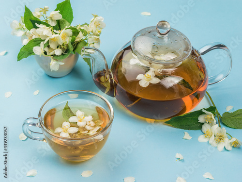 Glass teapot and glass glass with jasmine tea on a blue background.