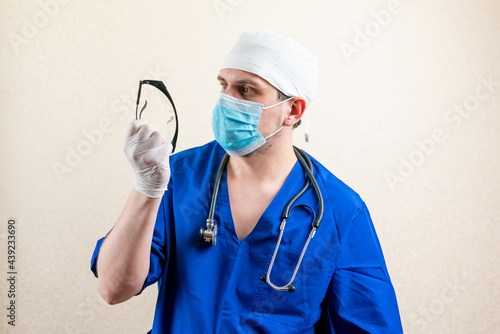 Doctor in a mask with a stethoscope in his hands. On a light background.