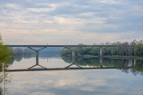 the bridge over the river is reflected in the water against the background of clouds