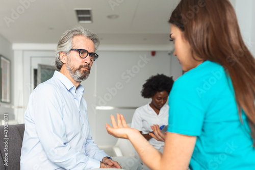 Young female doctor and senior man communicating in a waiting room at hospital. medicine  healthcare and people concept - doctor and patient meeting at hospital
