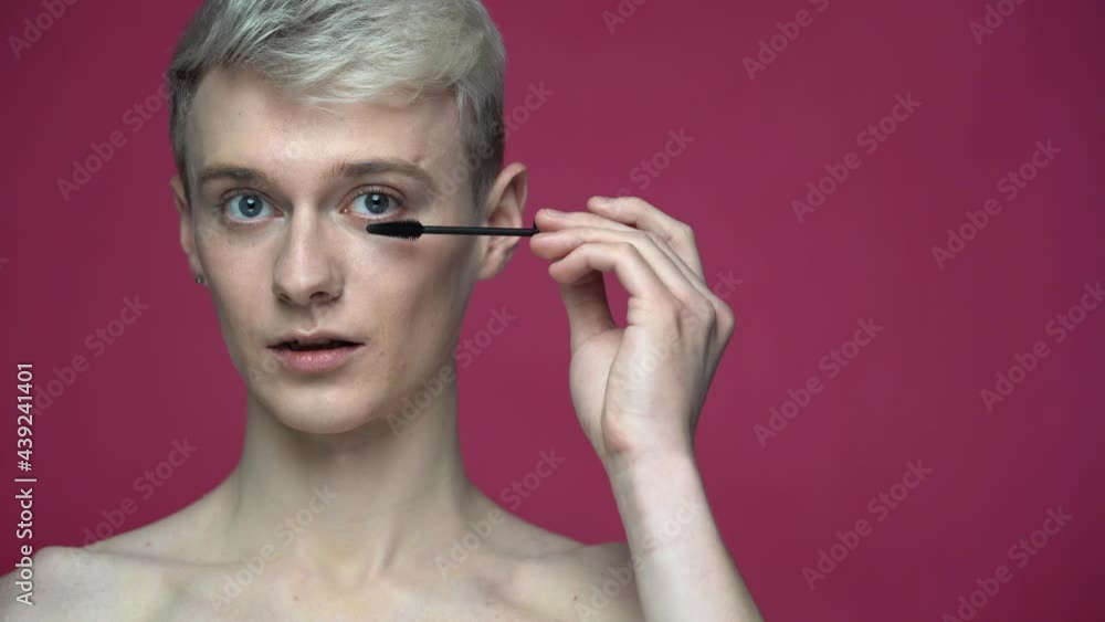 Portrait of smiling topless transgender doing make up with eyelash mascara isolated on red background Portrait of smiling topless transgender doing make up with eyelash mascara isolated on red background