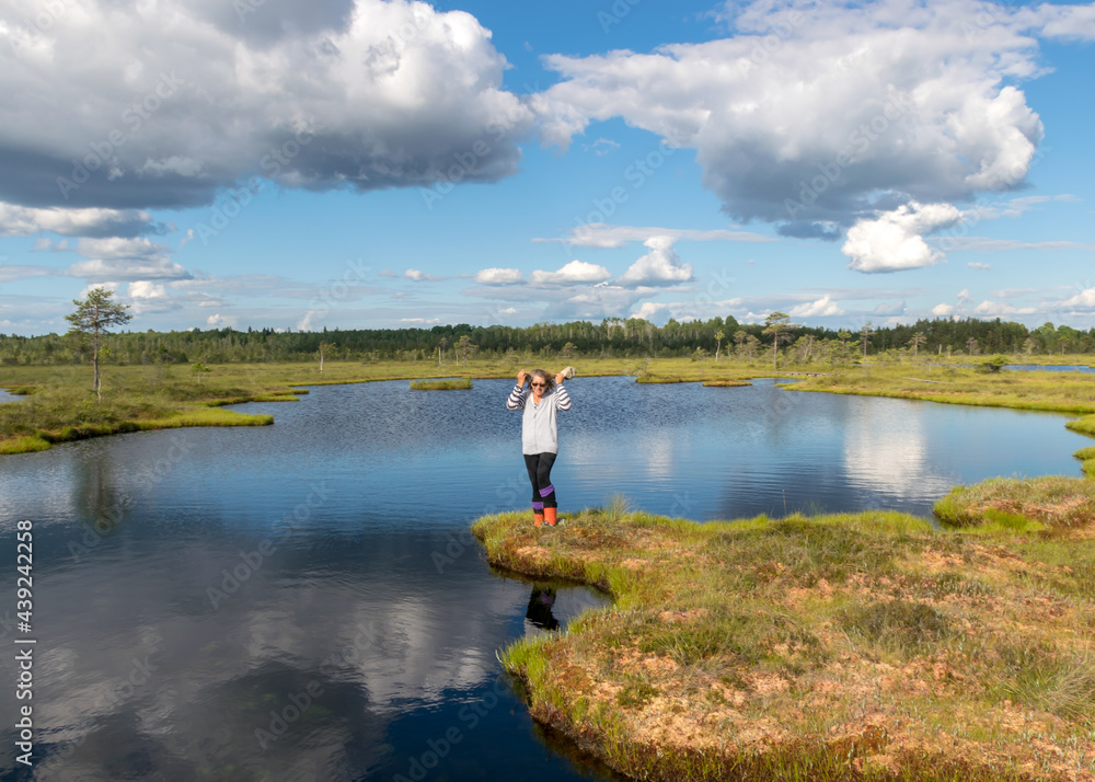 swamp landscape with blue sky and water, woman enjoys swamp landscape, hike with snowshoes in swamp, traditional swamp plants, mosses and trees, bog in summer
