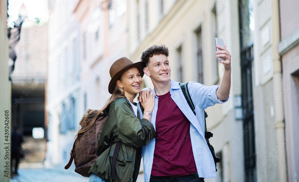 Young couple travelers with smartphone sightseeing in city on holiday, taking selfie.