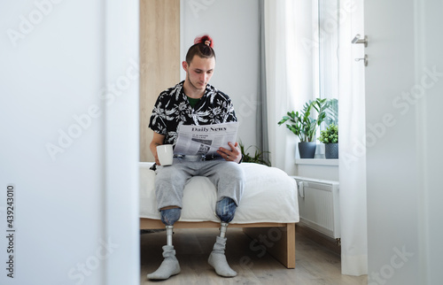 Portrait of disabled young man reading newspapers on bed indoors at home, leg prosthetic concept. © Halfpoint
