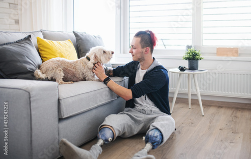 Portrait of disabled young man playing with dog indoors at home, leg prosthetic concept Fototapet