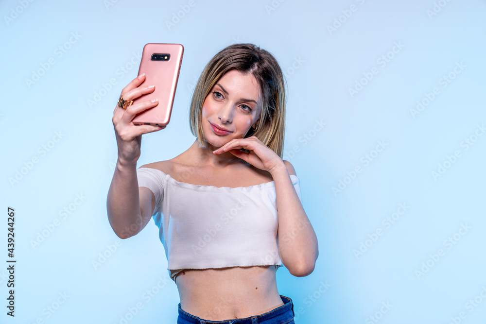 Photo of young caucasian girl with light blue eyes who takes selfie with her smartphone - Studio photography of pretty woman holding her phone photographing herself Photo of young caucasian girl with light blue eyes who takes selfie with her smartphone - Studio photography of pretty woman holding her phone photographing herself