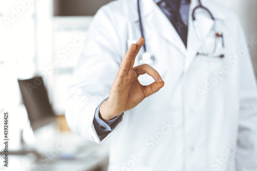 Unknown male doctor standing straight with OK sign in clinic near his working place, closeup. Perfect medical service in hospital. Medicine and healthcare concept