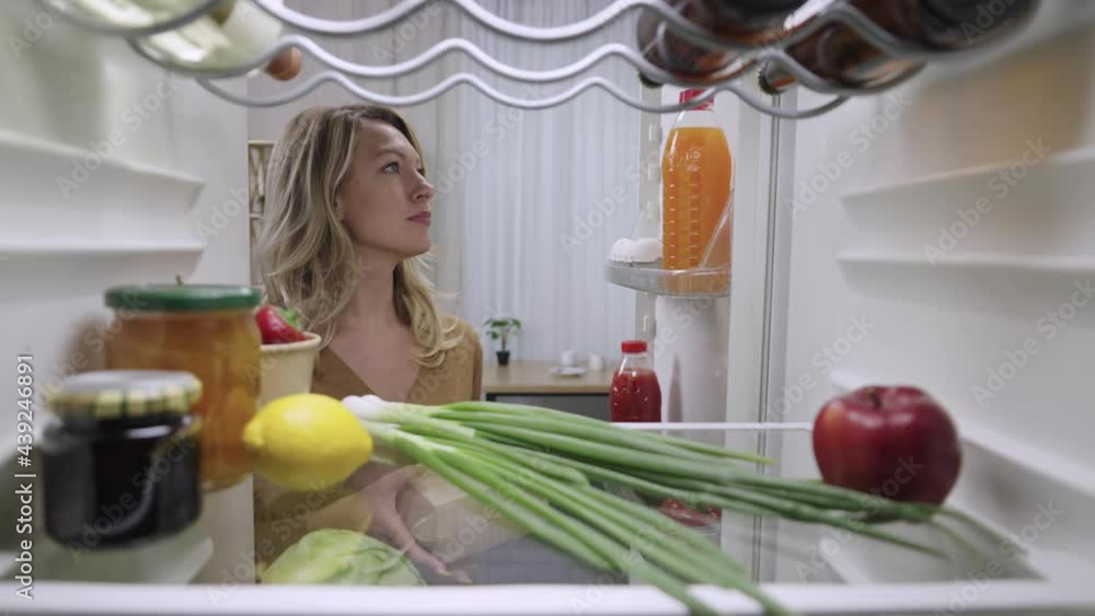 Young woman opens the refrigerator door and takes out a burger box and juice. Hungry blonde girl is about to have dinner. View from inside fridge. Close up. Slow motion ready 59.94fps. Young woman opens the refrigerator door and takes out a burger box and juice. Hungry blonde girl is about to have dinner. View from inside fridge. Close up. Slow motion ready 59.94fps.