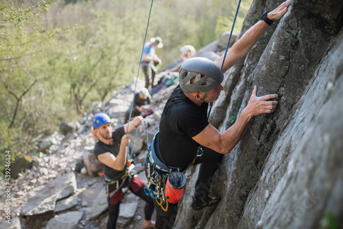 Senior man with instructor climbing rocks outdoors in nature, active lifestyle.