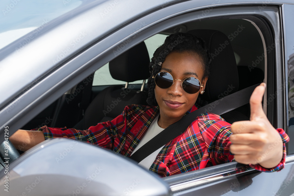 Naklejka premium Smiling afro american woman doing a thumbs up gesture in her car: Selective focus. Driving concept.