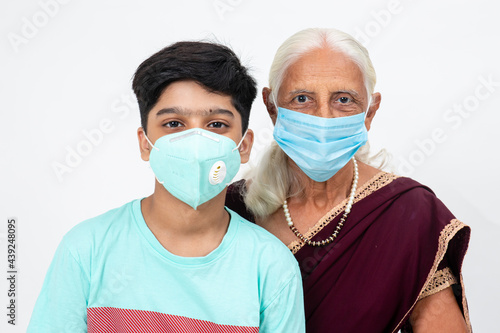 Young Indian boy stands with his grand mother both wearing Covd-19 protection mask, Senior Indian female with her grandson.