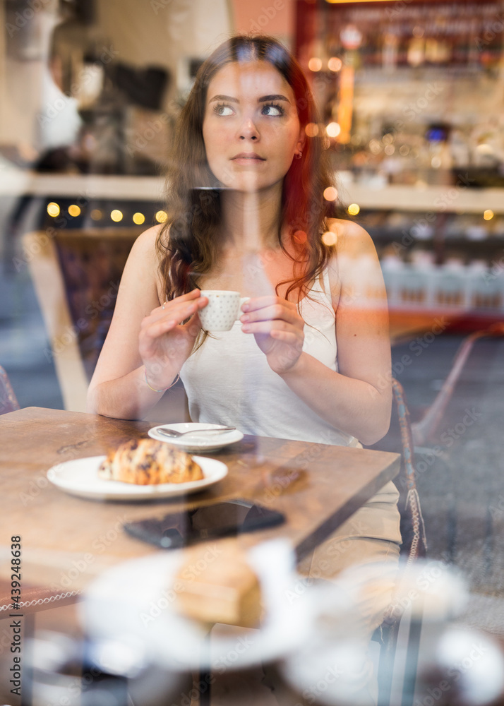 Portrait of young female at table in a cafe, drinking coffee from a cup