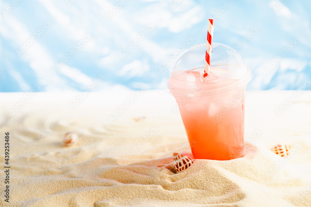 Cold tropical fruit cocktail in transparent plastic glass takeaway with straw on sunny coast with sand, ocean view. Bright hot summer beach holiday.
