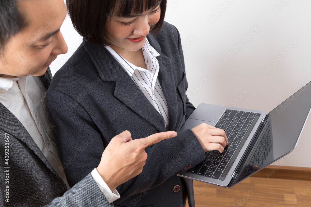 Young Asian businesswoman and businessman working together with laptop computer, holding computer in office room.