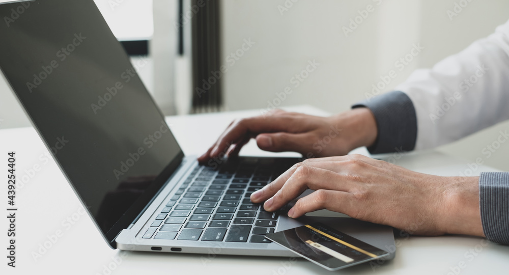 The businessman's hand is holding a credit card and using a laptop for online shopping and internet payment The businessman's hand is holding a credit card and using a laptop for online shopping and internet payment
